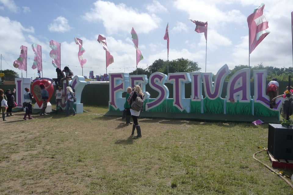 Un campo cubierto de césped con un cartel grande que dice "FESTIVAL" y varias banderas.