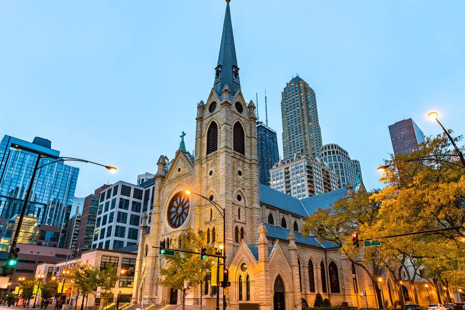 A historic church with a tall spire, surrounded by modern high-rise buildings.