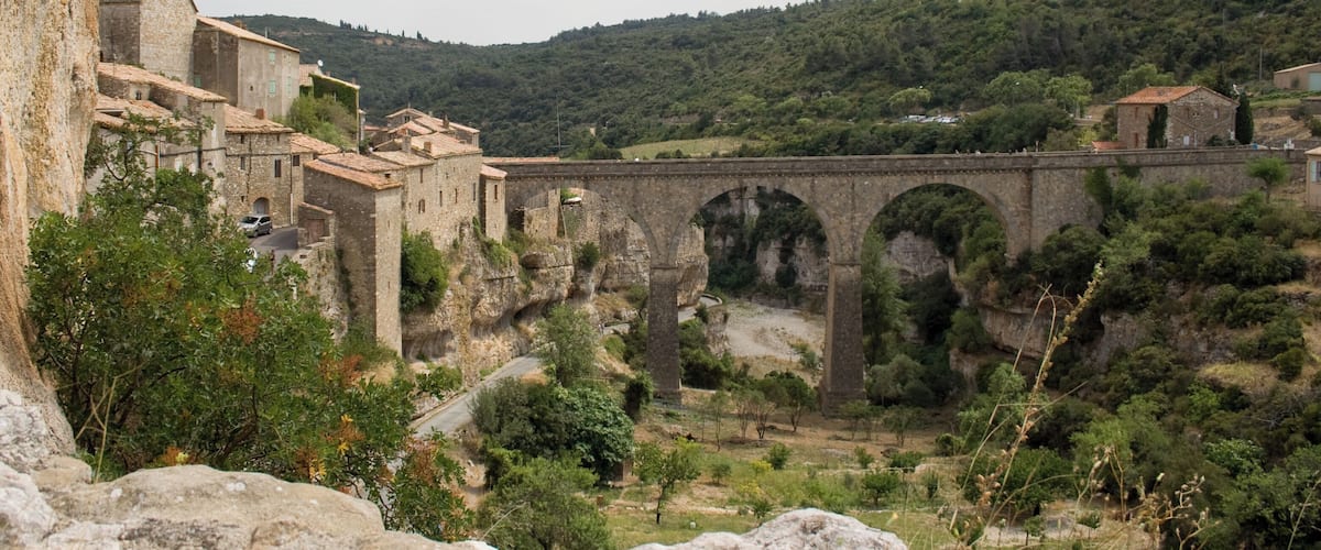 A stone bridge with arches over a valley, surrounded by greenery and historic buildings.