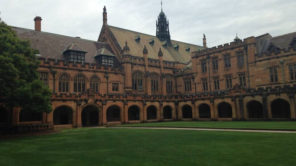 A historic building with arched walkways and a large lawn.