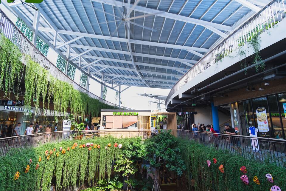 An indoor shopping mall with a high ceiling, greenery, and a food court area.