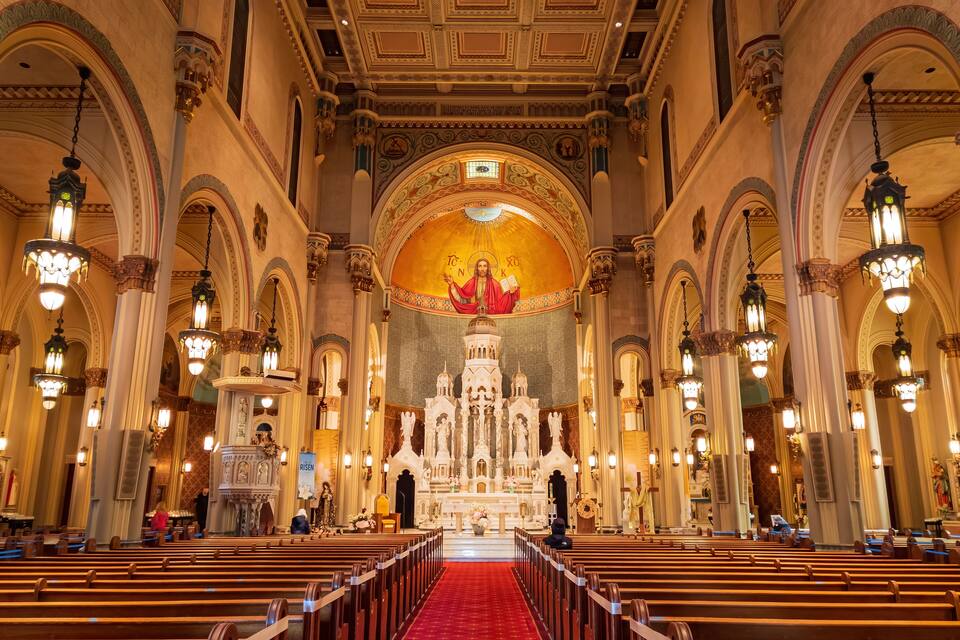 A church interior with ornate columns, a red carpet, and a central altar.