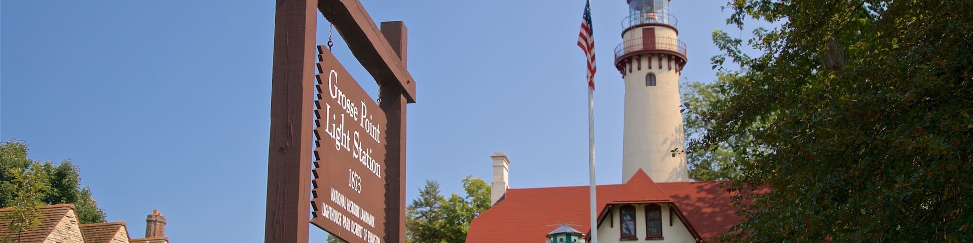 A historic lighthouse, a stone building, and a sign indicating the Grosse Pointe Light Station from 1875.