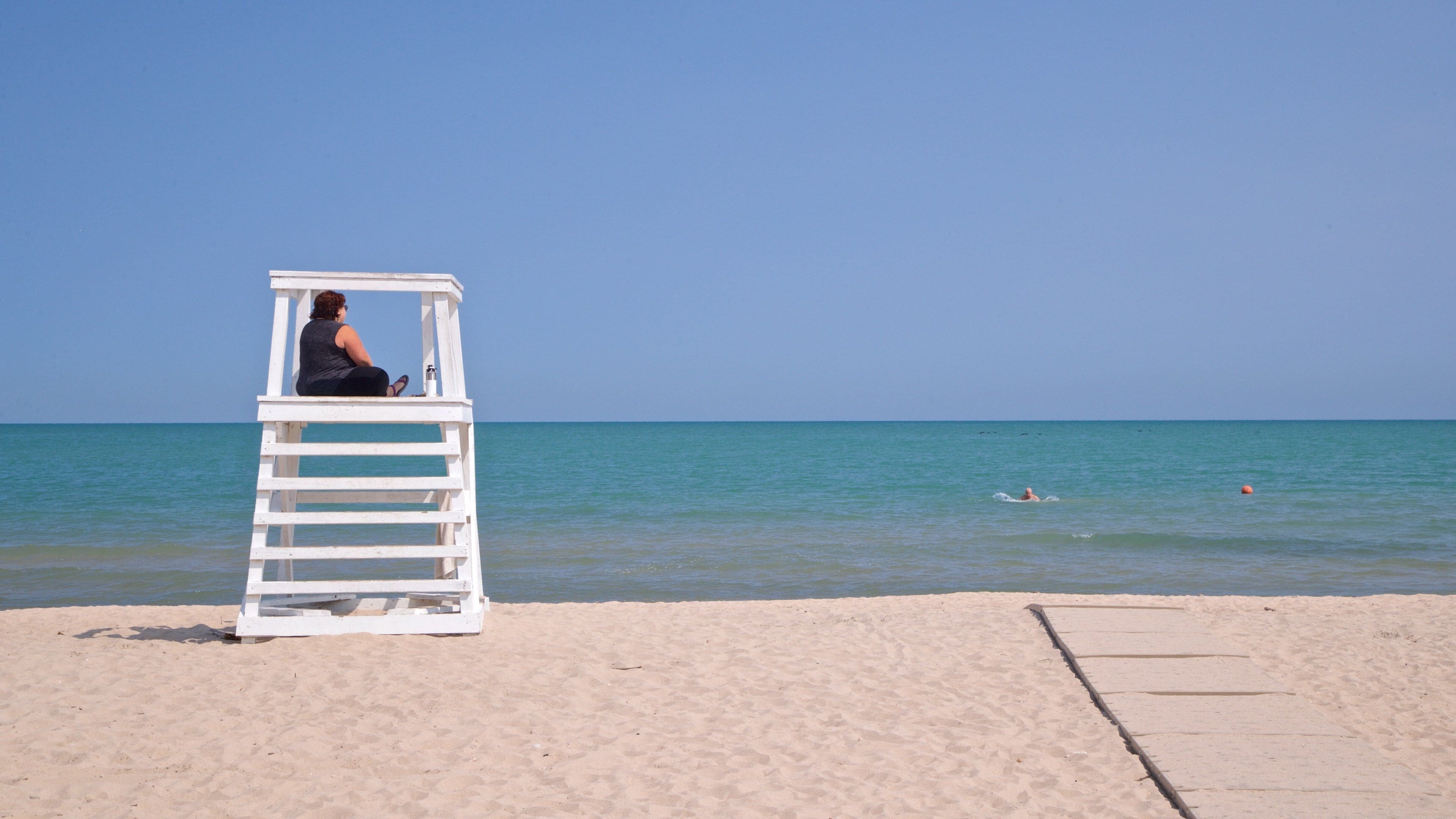 A lifeguard tower on a sandy beach with calm blue waters and a clear sky.
