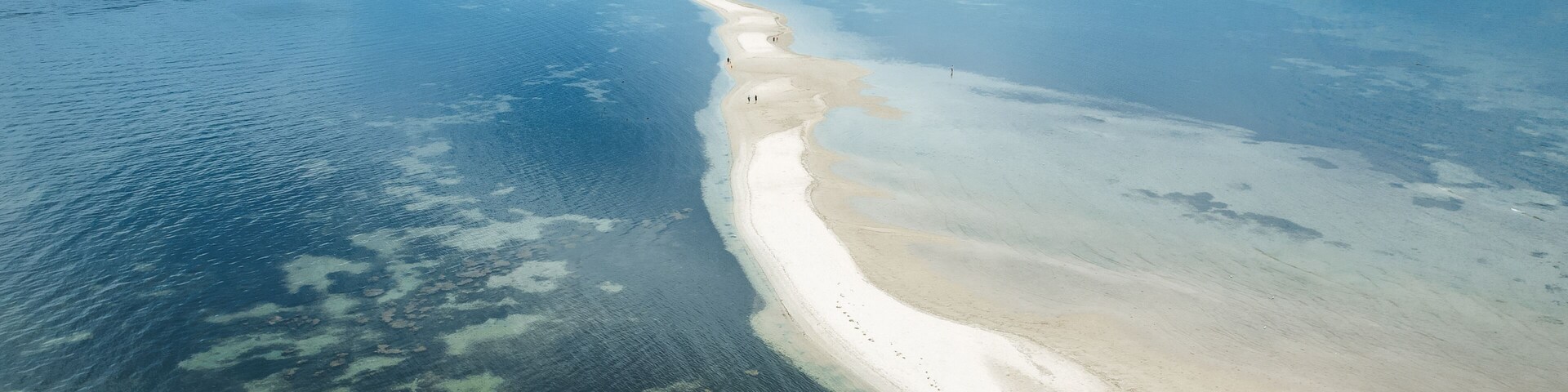 Vista aérea de una playa con aguas cristalinas, una costa arenosa y un horizonte urbano distante.