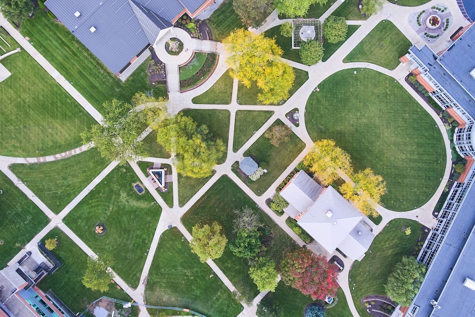 An aerial view of a park with green lawns, trees, a circular plaza, and buildings.