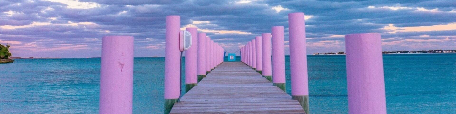 A wooden pier leading to a beach with pink posts, under a cloudy sky.