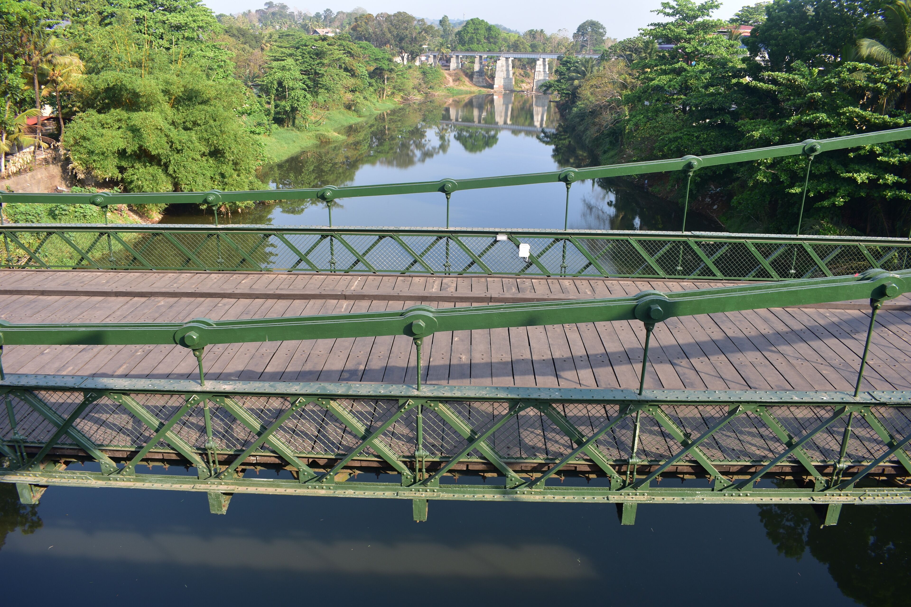 A green metal bridge over a calm river with lush greenery on both sides.