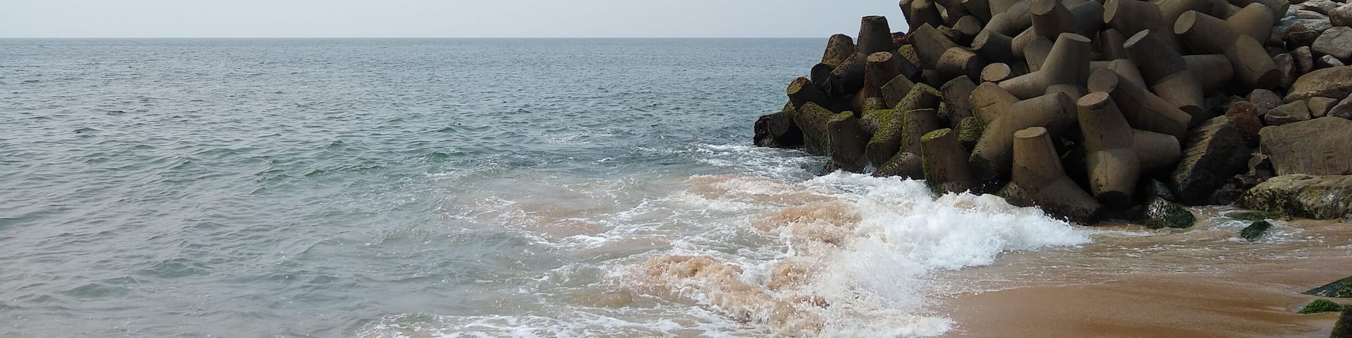 A beach with waves crashing onto the shore and a pile of cylindrical concrete structures.