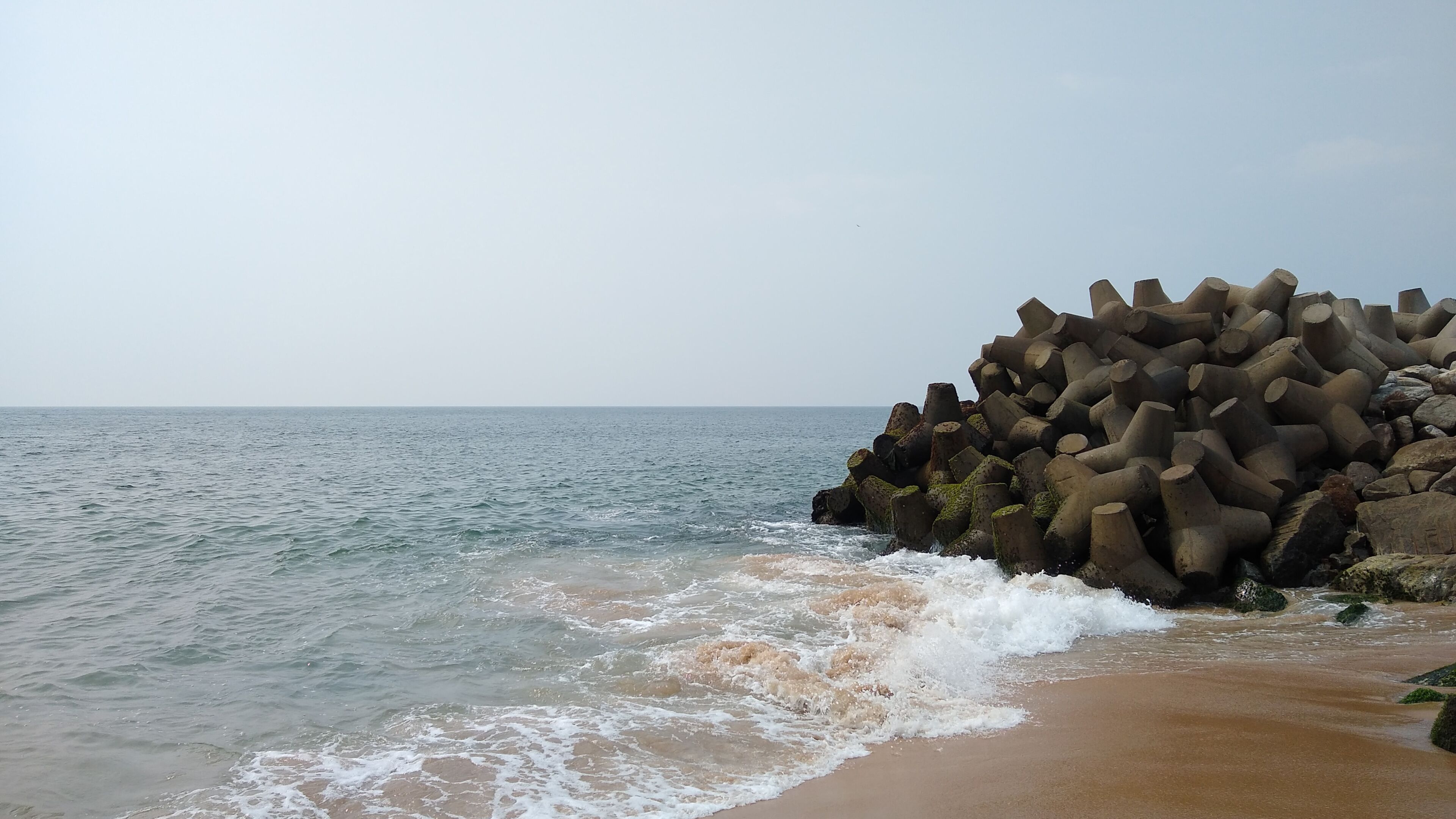 A beach with waves crashing onto the shore and a pile of cylindrical concrete structures.