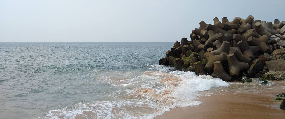 A beach with waves crashing onto the shore and a pile of cylindrical concrete structures.