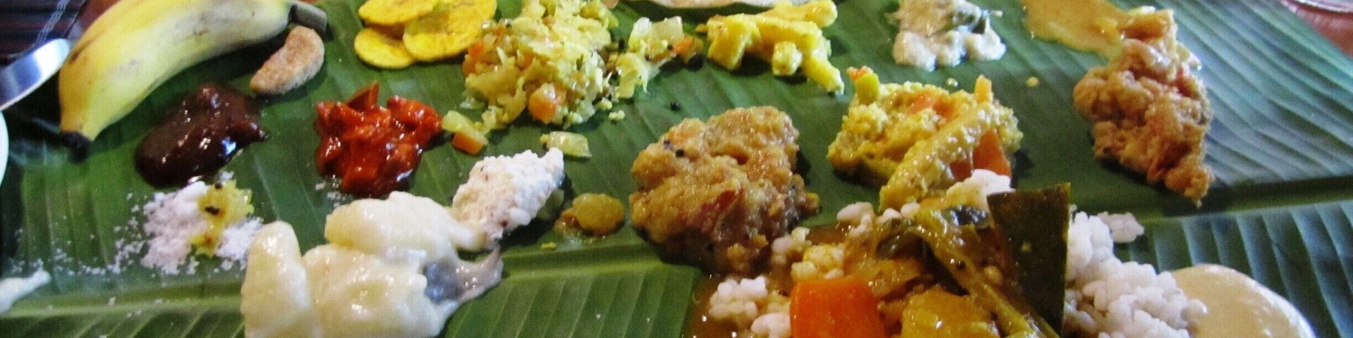 Variedad de platos servidos sobre hojas de plátano, incluyendo arroz, verduras y posiblemente carne.
