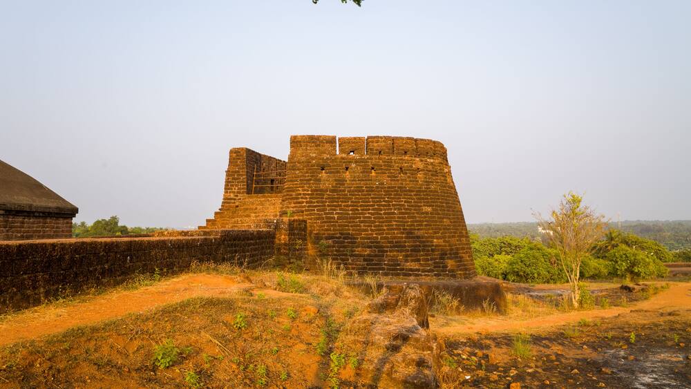 An ancient brick fort with a large wall and a smaller tower, surrounded by dry grass and sparse vegetation.