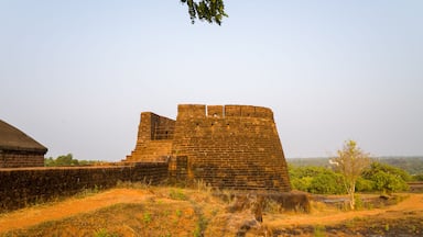 Una antigua fortaleza de ladrillo con un muro grande y una torre más pequeña, rodeada de hierba seca y vegetación escasa.