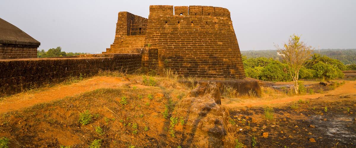 An ancient brick fort with a large wall and a smaller tower, surrounded by dry grass and sparse vegetation.