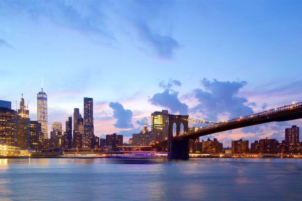 A city skyline with illuminated buildings and a bridge over a body of water.