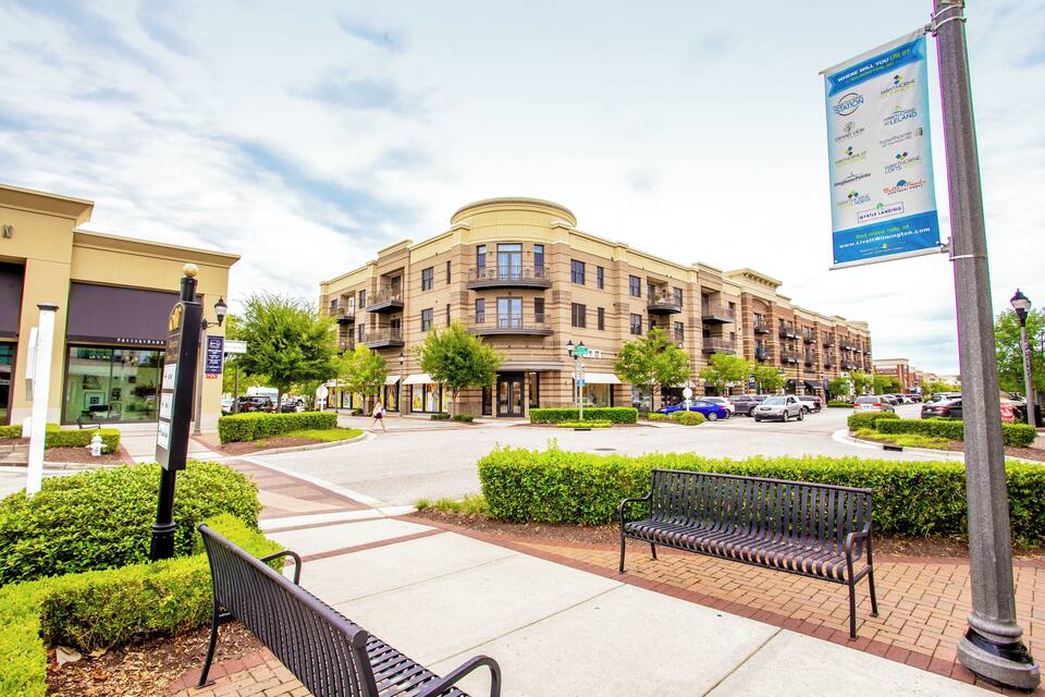 A multi-story building with a curved facade, benches, and a street with cars and pedestrians.