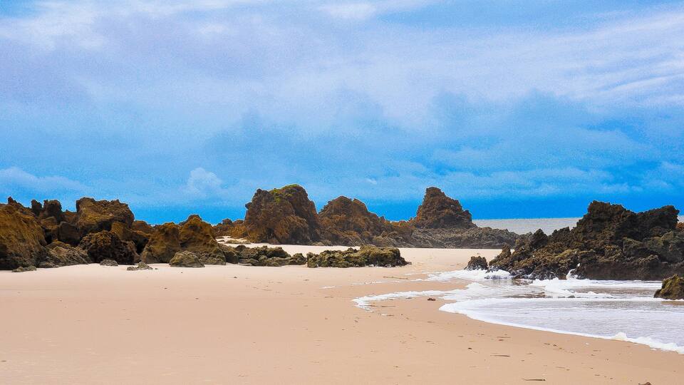 A sandy beach with large rock formations and waves crashing onto the shore.