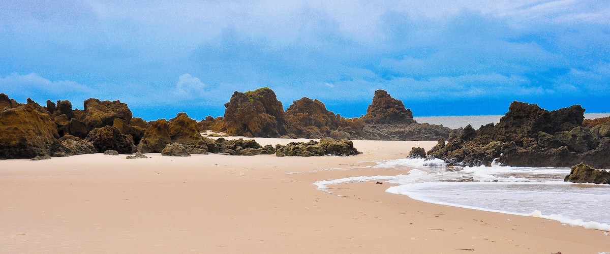 A sandy beach with large rock formations and waves crashing onto the shore.