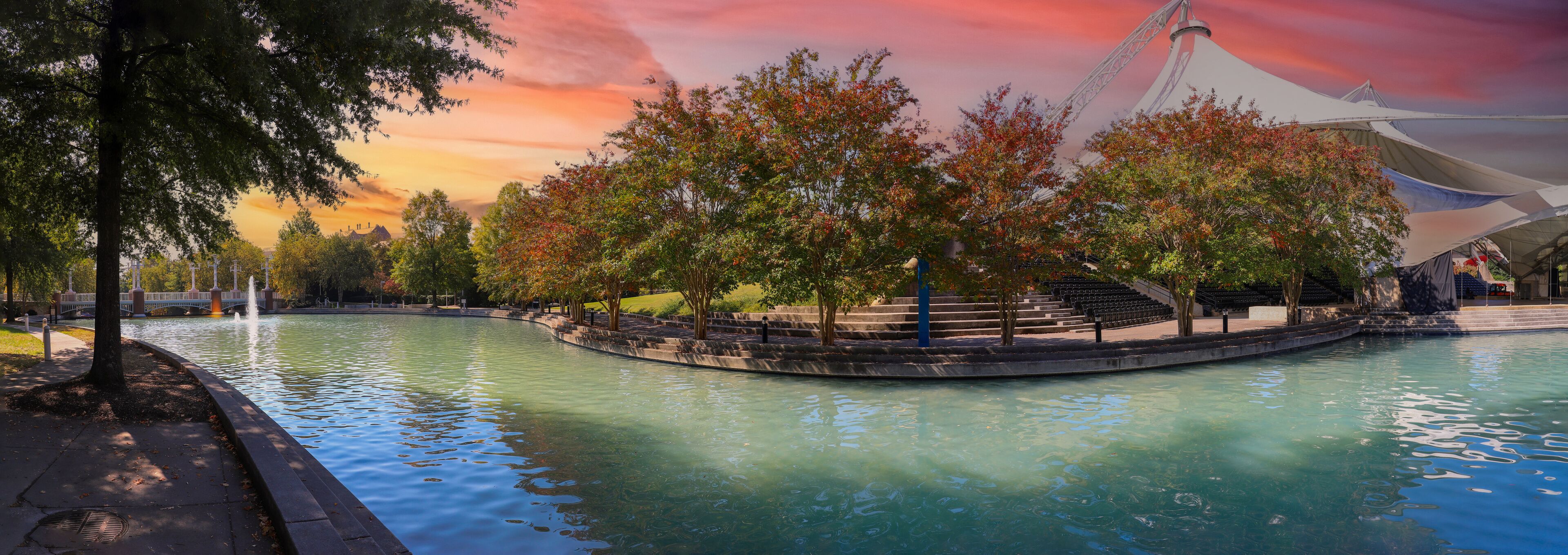 a stunning autumn landscape at World's Fair Park with a pool with blue water surrounded by red and yellow autumn trees and lush green trees and plants with a red sky at sunset in Knoxville