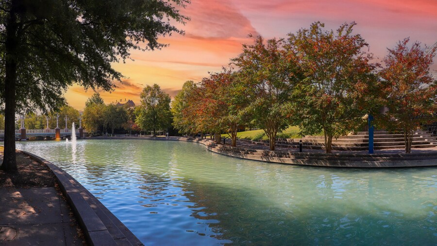 a stunning autumn landscape at World's Fair Park with a pool with blue water surrounded by red and yellow autumn trees and lush green trees and plants with a red sky at sunset in Knoxville