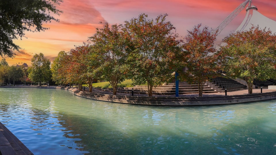A riverside park with trees, a bridge, and a modern structure.
