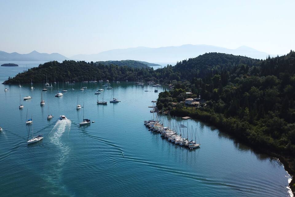 A coastal bay with numerous sailboats anchored near a forested island.