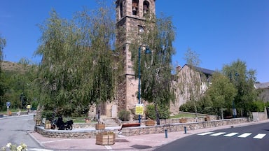 A historic church with a tall bell tower, surrounded by trees and a street with a crosswalk.