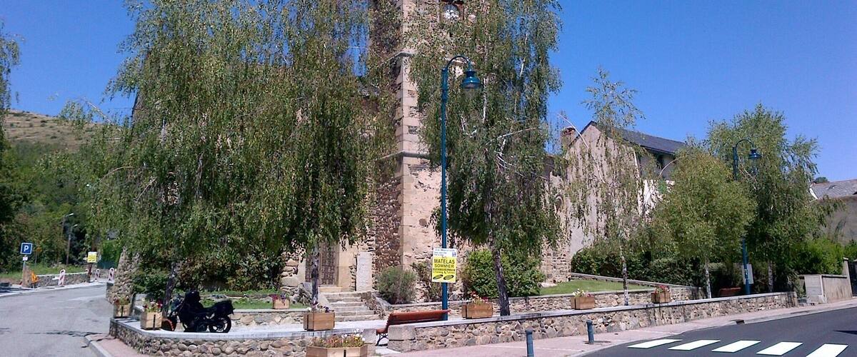 A historic church with a tall bell tower, surrounded by trees and a street with a crosswalk.