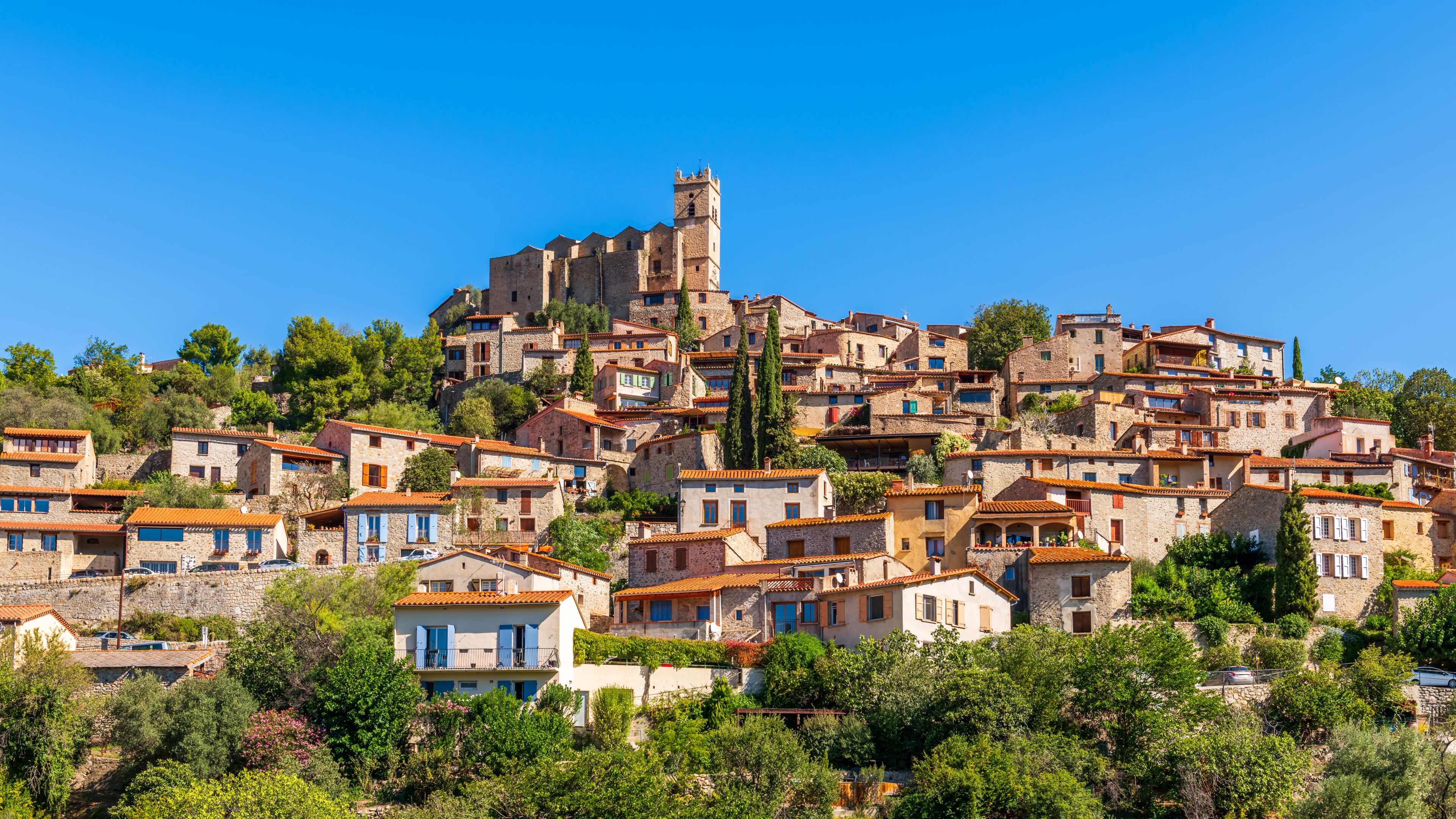 A hillside village with stone buildings, a prominent tower, and lush greenery.