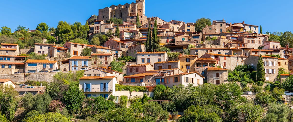 A hillside village with stone buildings, a prominent tower, and lush greenery.