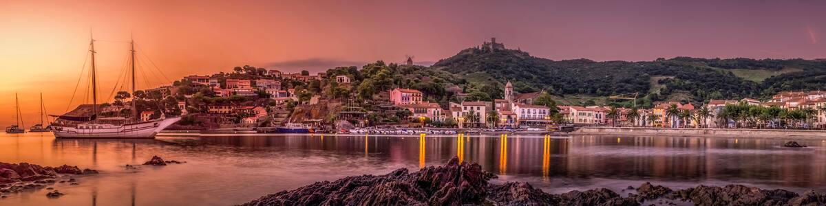 A coastal town at sunset with a prominent hill and a windmill.