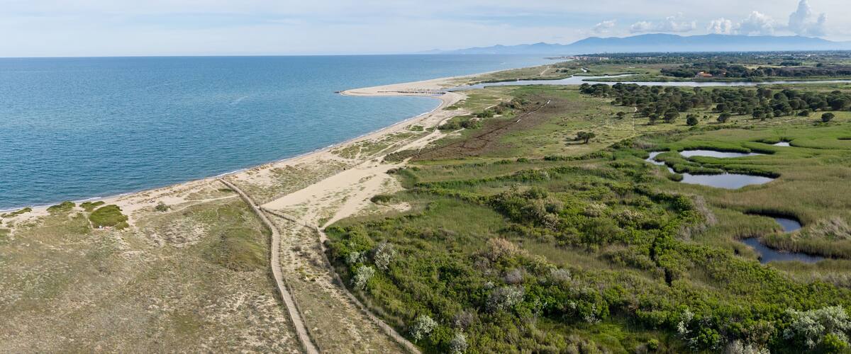 A coastal landscape with a sandy beach, grassy areas, and a series of small ponds.