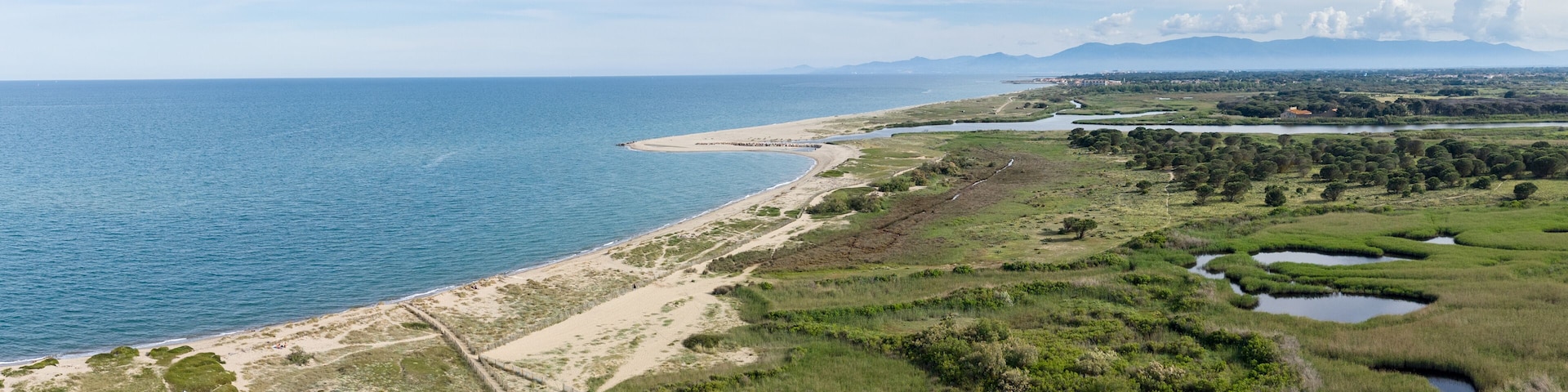 A coastal landscape with a sandy beach, grassy areas, and a series of small ponds.
