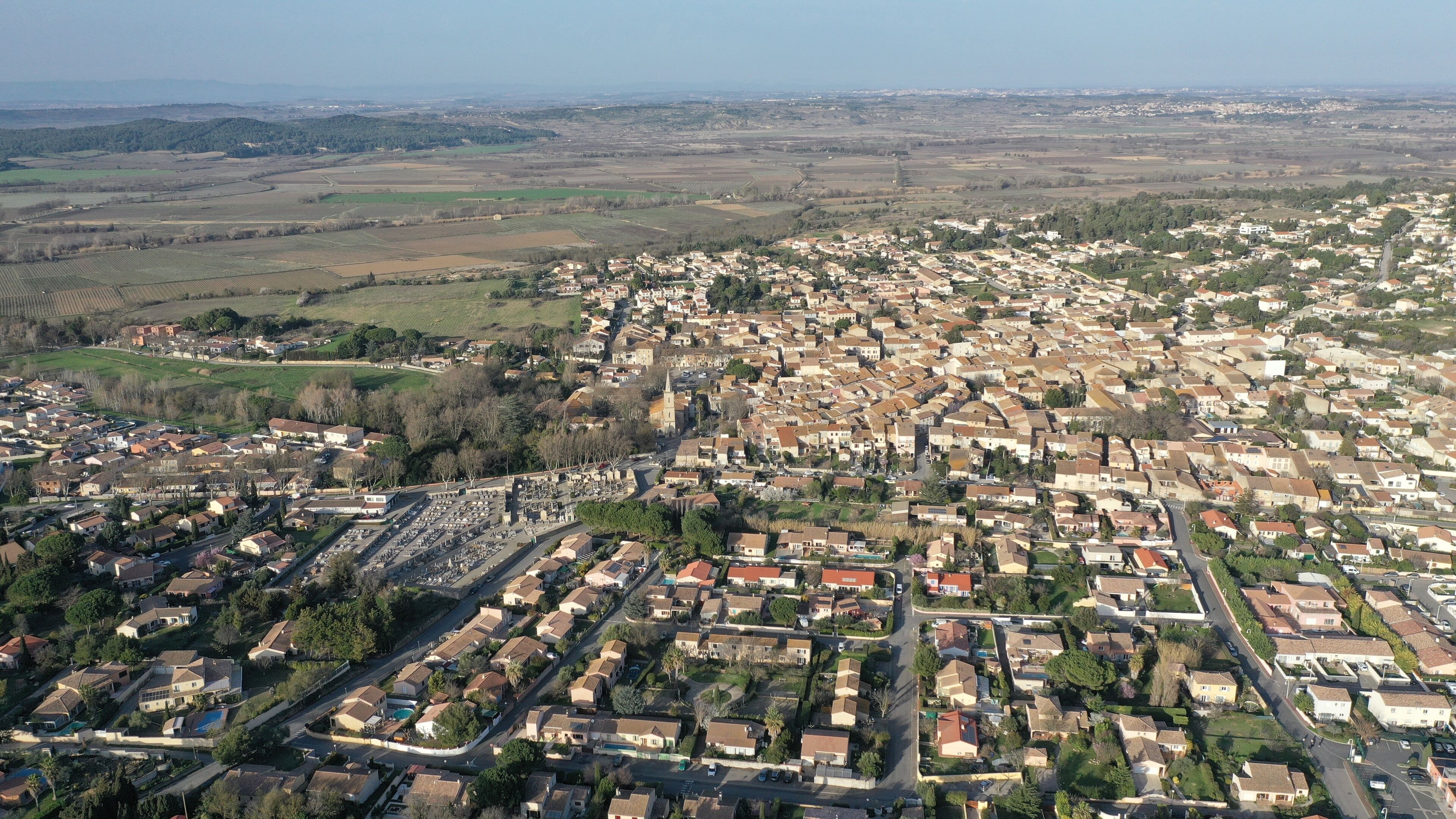An aerial view of a densely populated town with a mix of residential buildings, a prominent church, and surrounding agricultural fields.