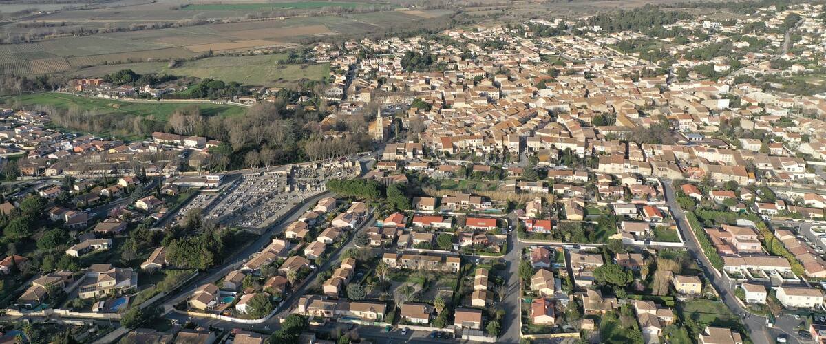 An aerial view of a densely populated town with a mix of residential buildings, a prominent church, and surrounding agricultural fields.