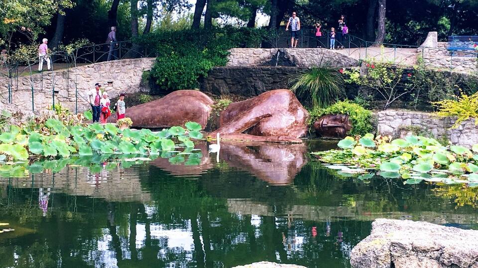 A pond with large rocks, lily pads, and a stone bridge.