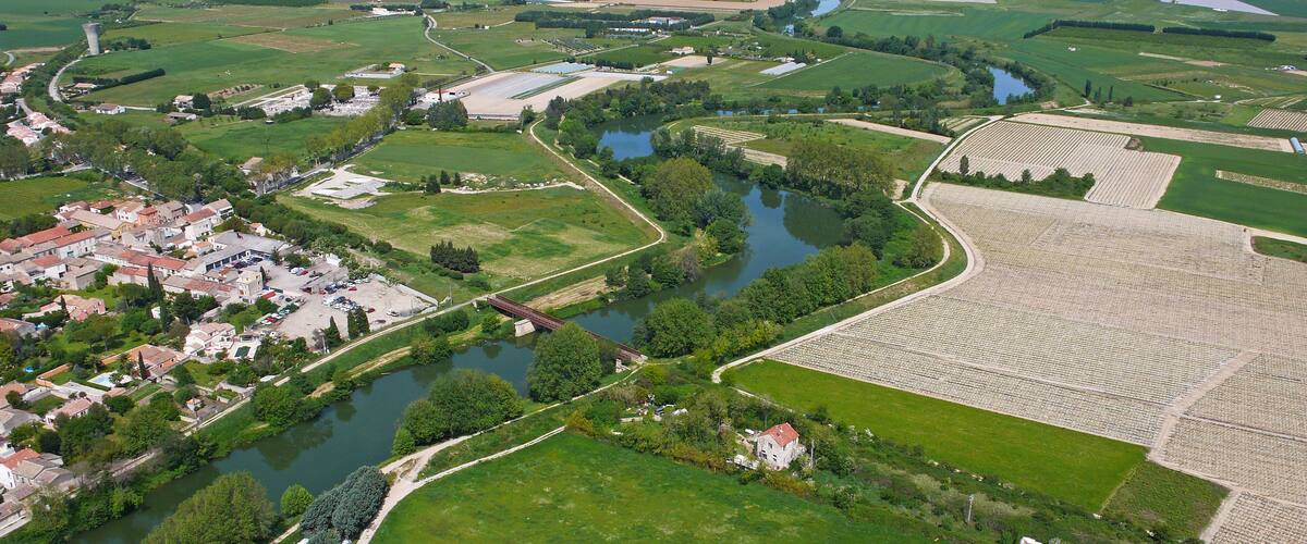 An aerial view of a town with a river, green fields, and a bridge.