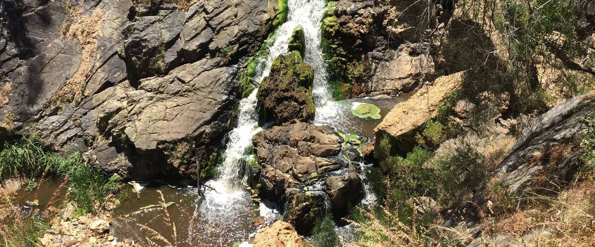 A waterfall cascading over rocky terrain with sparse vegetation.
