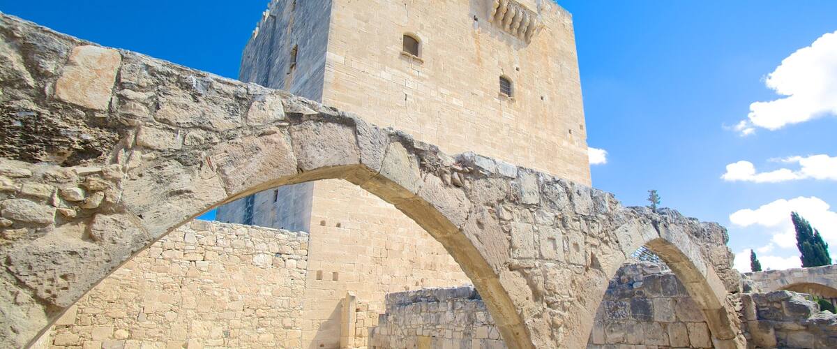 An ancient stone bridge with arches leading to a tall, fortified tower under a clear blue sky.