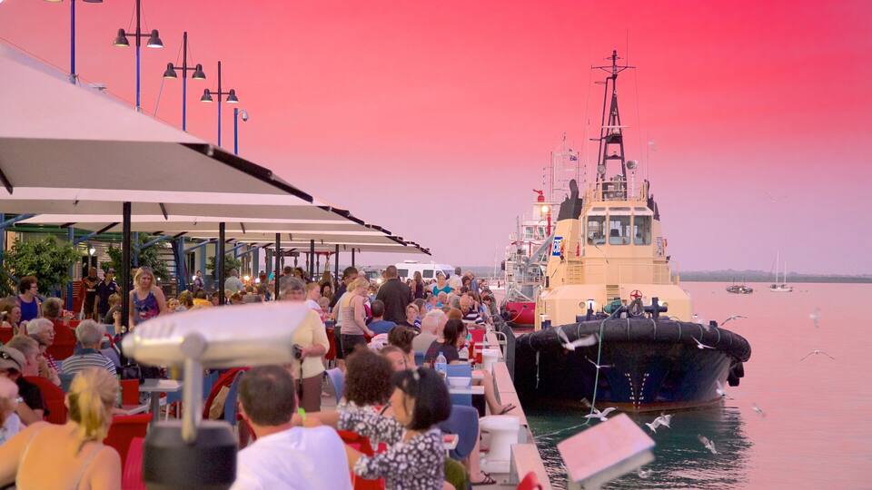 A crowded pier with people dining and a large ship docked in the background.
