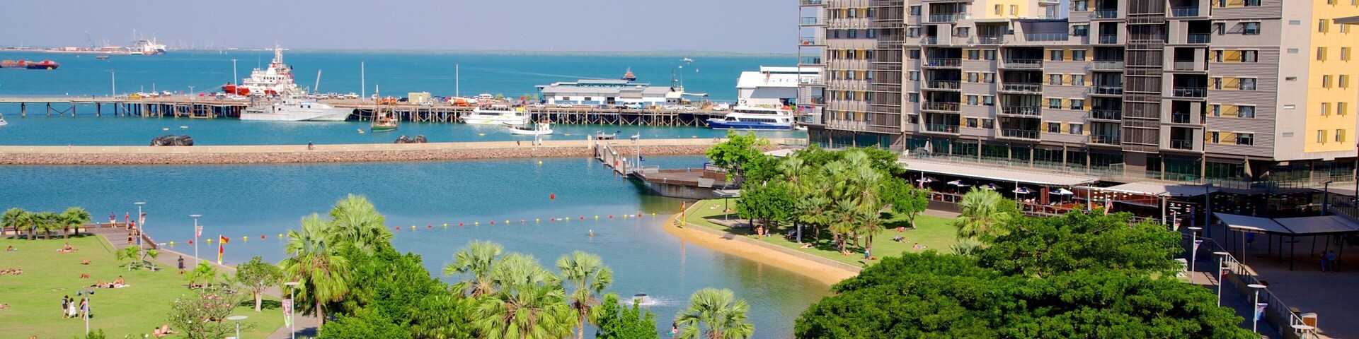 Un paisaje urbano costero con un puerto deportivo, edificios modernos y un parque con palmeras.