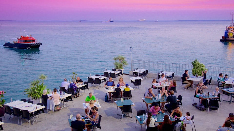 A coastal dining area with tables and chairs overlooking the sea, with ships in the background.