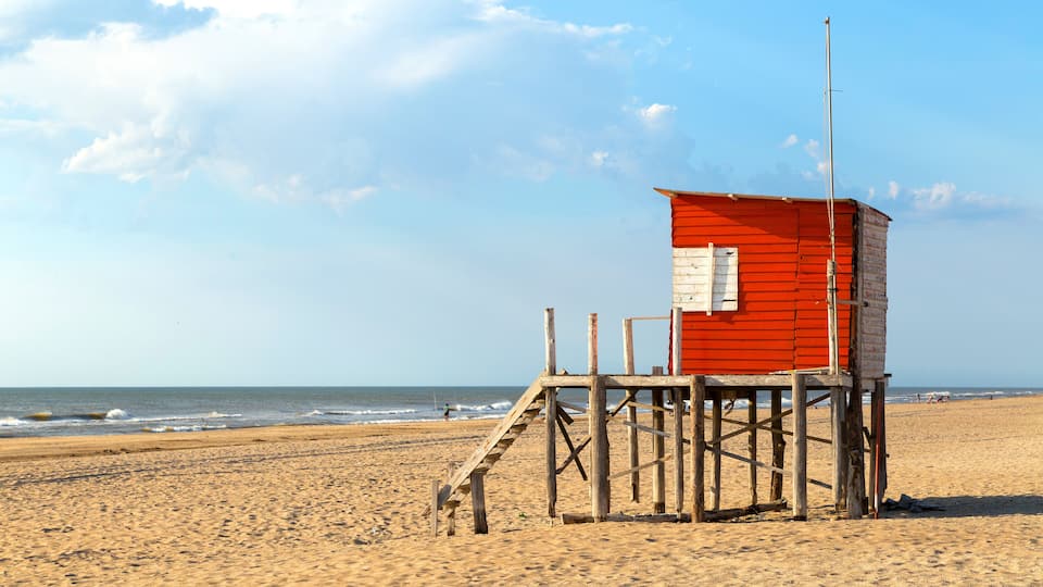 A red lifeguard tower on a sandy beach with the ocean in the background.