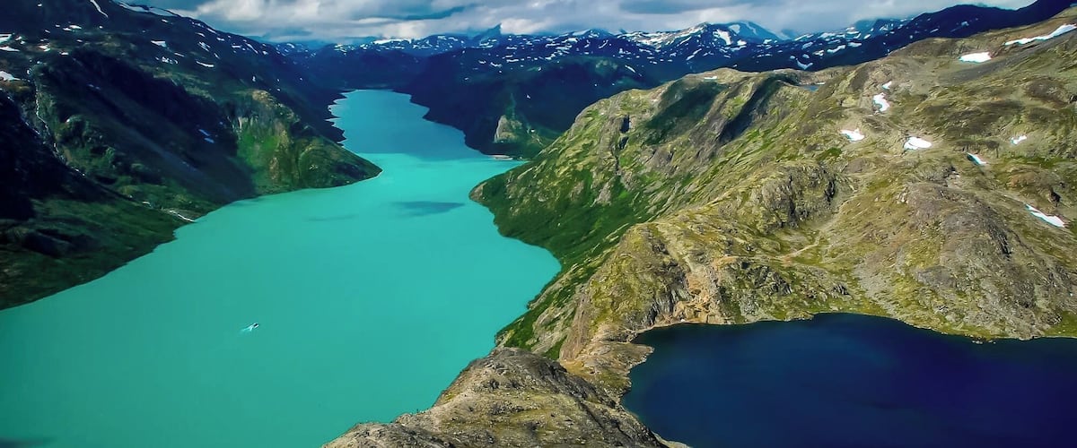 A turquoise lake surrounded by rugged mountains with patches of snow.