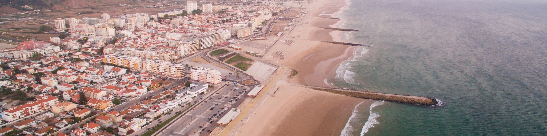 Vista aérea de una ciudad costera con una playa extensa, un muelle que se adentra en el mar y un desarrollo urbano denso.