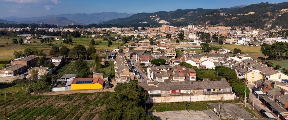 A town with a mix of residential and commercial buildings, surrounded by green fields and mountains in the background.