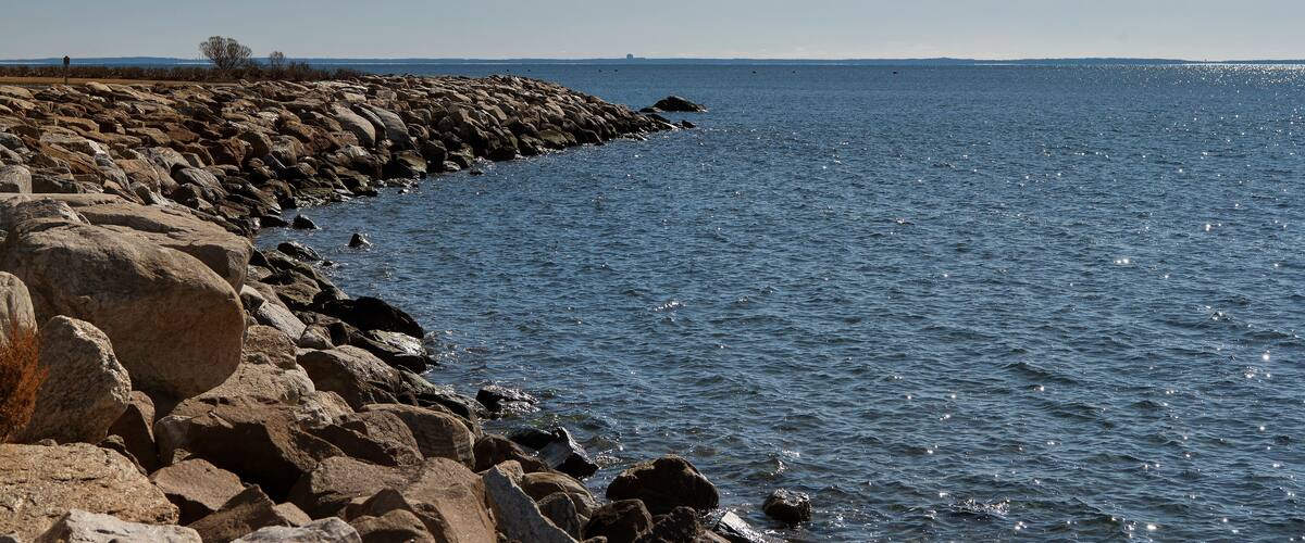 A rocky shoreline with calm water and a clear sky.