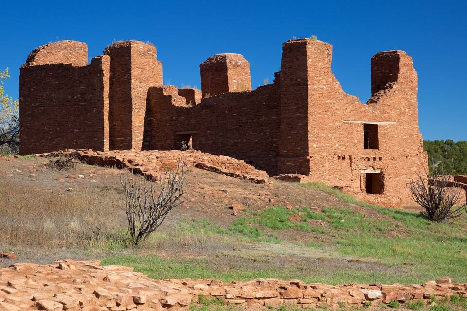 A large, ancient brick structure with multiple towers and walls, surrounded by a grassy landscape and sparse vegetation.