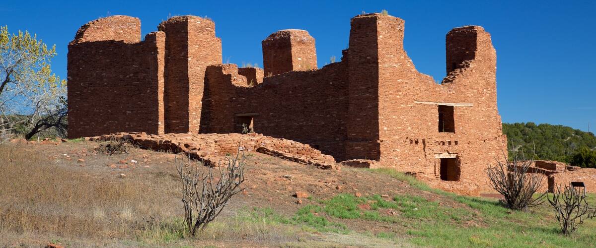 A large, ancient brick structure with multiple towers and walls, surrounded by a grassy landscape and sparse vegetation.